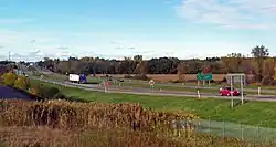 A divided highway going across a level landscape. On the right is a sign in English and French saying "Last U.S. Exit/Derniere Sortie EE. U." On the left the road goes away from the camera, up a slight rise to a more built-up area with a tall antenna.