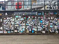 An informal shrine labelled "Ianto's Shrine", with many notes, pictures, and other objects on a brown wall.