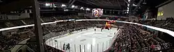 A panoramic view of a hockey rink with a large inflatable dragon head on the ice