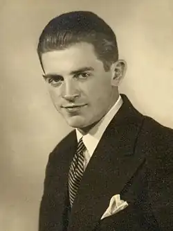 Jānis Daliņš shown from about the chest up in a suit jacket and tie.