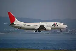 A Boeing 737-400 aircraft painted in new JAL corporate livery with a skyline background