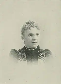 B&W portrait photo of a middle-aged woman with her hair in an up-do, wearing a high-collared dark blouse.