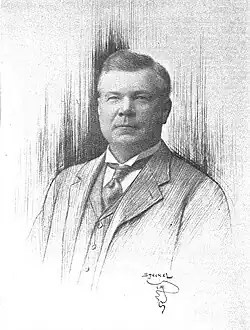 A man with a round face wearing an early 20th century suit and tie