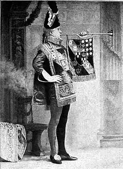 Tall, clean shaven white man in herald's tabard, blowing long trumpet