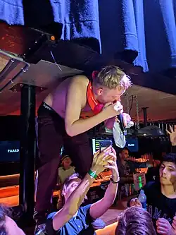 Photo of Joost Klein standing on a bar, not wearing a short, holding a microphone