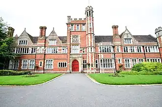 A mock tudor, red brick building with crenellations in white stone and a central tower.