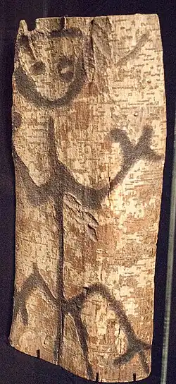 A wooden plank displaying an artistic carving of a human-like figure, representing an ancestor of the Moriori people.