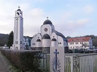 Modern monastery building with white walls and bell tower surrounded by trees