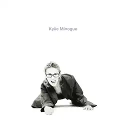 A black and white picture of Minogue licking her lips, crouching low, wearing suits and a pair of glasses