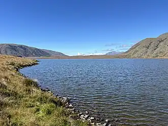 A lake surrounded by mountains on a clear day, with a grassy shoreline
