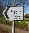 Vandalism on a street sign, making it read "I Swim in Poo nmunit en re"