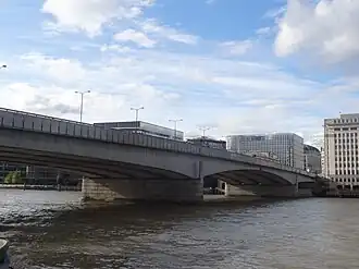 Wide bridge over water against a grey sky with tall buildings