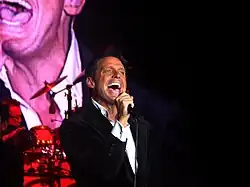 A man is facing right while holding a microphone with his right hand.