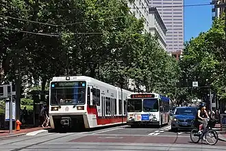 Photograph of a Max train on the left, a bus in the center and a woman on a bicycle making a turn off the Portland Transit Mall