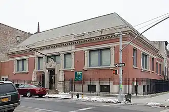 A square two-story brick building stands before a snowy sidewalk against a gray sky.