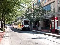 A MAX train approaching the platform of Mall/Southwest 5th Avenue station with a passenger waiting to board