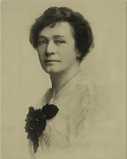 B&W portrait photo of a woman with short wavy hair wearing a white blouse with a large dark bow.