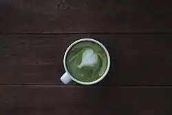 A white mug of matcha green tea with a heart made in latte art in it, viewed from above.