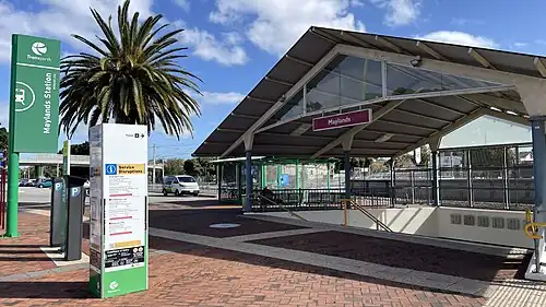 An entrance with a staircase down to a pedestrian underpass, with the station platform behind
