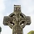Circa 922 A.D., Ireland. Muiredach's High Cross: Christ (center), David plays the harp (left) with a trumpet and singers behind him; a man plays the triple pipes (right) with a devil driving away condemned souls behind him.