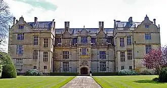Facade of house built of yellow stone. Three floors with large, mullioned windows and Dutch gables to the roof.
