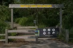 Facing the wooden entrance gate which has a sign that displays the name "Montrose Point Bird Sanctuary" in yellow letters above the entrance, and rules to the side.