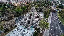 Aerial view of a Mesoamerican-like pyramid. It is three-stories high. On top, an eagle spreads its wings.