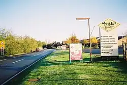 A sign for the Moss End Garden Village next to the road