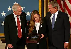 A color image of Murphy's parents standing next to President George Bush in front of an American flag. They are holding Murphy's Medal of Honor in a display case and are looking down at it.