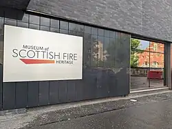 A white sign on a dark grey exterior wall which reads "Museum of Scottish Fire Heritage