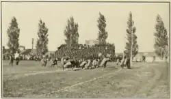 A tan and black blurry picture of two groups of men playing football with little protective equipment