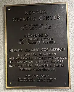A brass plaque reading: "Nevada Olympic Center. The contribution of the State of Nevada to the VIII Olympic Winter games. Governors: Hon. Grant Sawyer, Hon. Charles Russell. Nevada Olympic Commission: E.J. Questa. Chairman. William J. Cashill. Charles W. Mapes. Jr. Lee Frankovich. R. Julian Moore. John C. Kinnear. Francis R. Smith. George Wingfield. Jr. Advisory Board: William Berry, Chelton Leonard, Earl A. Edmunds, Gordon Wren."