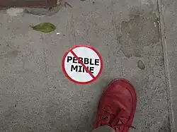Circular white sticker with "Pebble Mine" and a red line through it on a sidewallk
