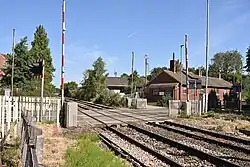 A level crossing with the barriers raised. Two buildings are in the background.