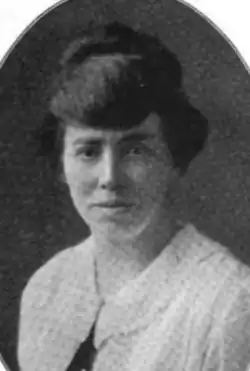 A white woman with dark hair in an updo, wearing a white blouse