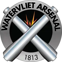 Distinctive unit insignia of the U.S. Army Watervliet Arsenal featuring a silver ring around two crossed cannons with a spark above where they cross signifying the manufacturing nature of the arsenal.