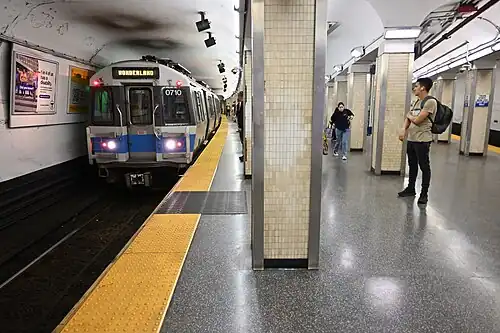 A subway train at an underground platform with white tiled columns