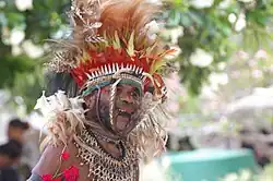 Man with a large feather headdress holding an animal jawbone in his mouth