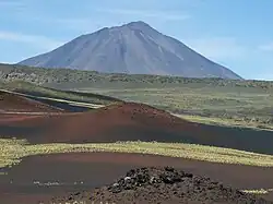 A volcanic cinder cone, with a conical mountain rising in the background