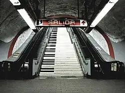 A staircase decorated as if each step was the key of a piano. It is located between two escalators.