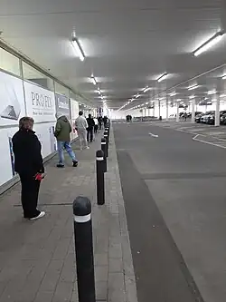 People queueing at an Irish supermarket, March 2020; strips of black tape on the ground to demarcate 2-metre gaps.