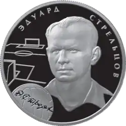 A silver coin with Strelstov's head and neck illustrated in relief upon it, accompanied by the outlines of a football pitch and a football and his name in Russian.