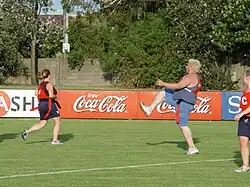 Three players in sports wear on a grassy field. One player has a foot in the air, as if they had just kicked a soccer ball.
