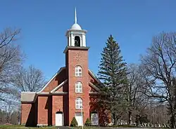 A brick building with a pine tree in front and a tower with white cupola