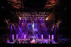 A wide shot photo of a concert stage with Velasquez performing wearing a red opera coat