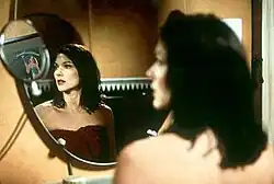 Laura Elena Harring wet from a shower and wrapped in a red towel, looking into the mirror at a reflection of the theatrical poster for the film Gilda