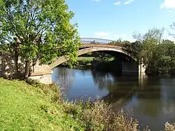 A cast iron bridge over a river surrounded by fields and trees
