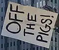 A sign reading “OFF THE PIGS” taped to the statue’s hand