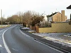 20th century suburban housing in a rural setting. A series of small, modern, houses on the right of a twisty road, with open views to the left.
