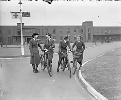A black and white image of four nursing sisters on pushbikes outside a hospital block